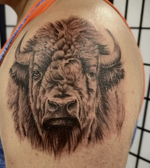 A bison head in black and grey realism on the shoulder.