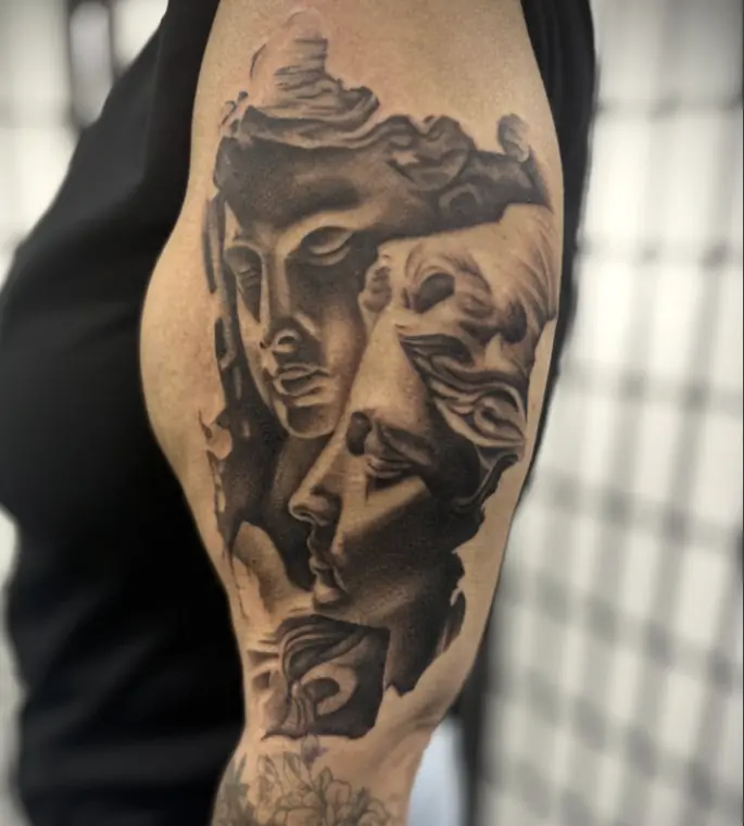 Two classical marble faces carved into an upper arm in black and grey realism.